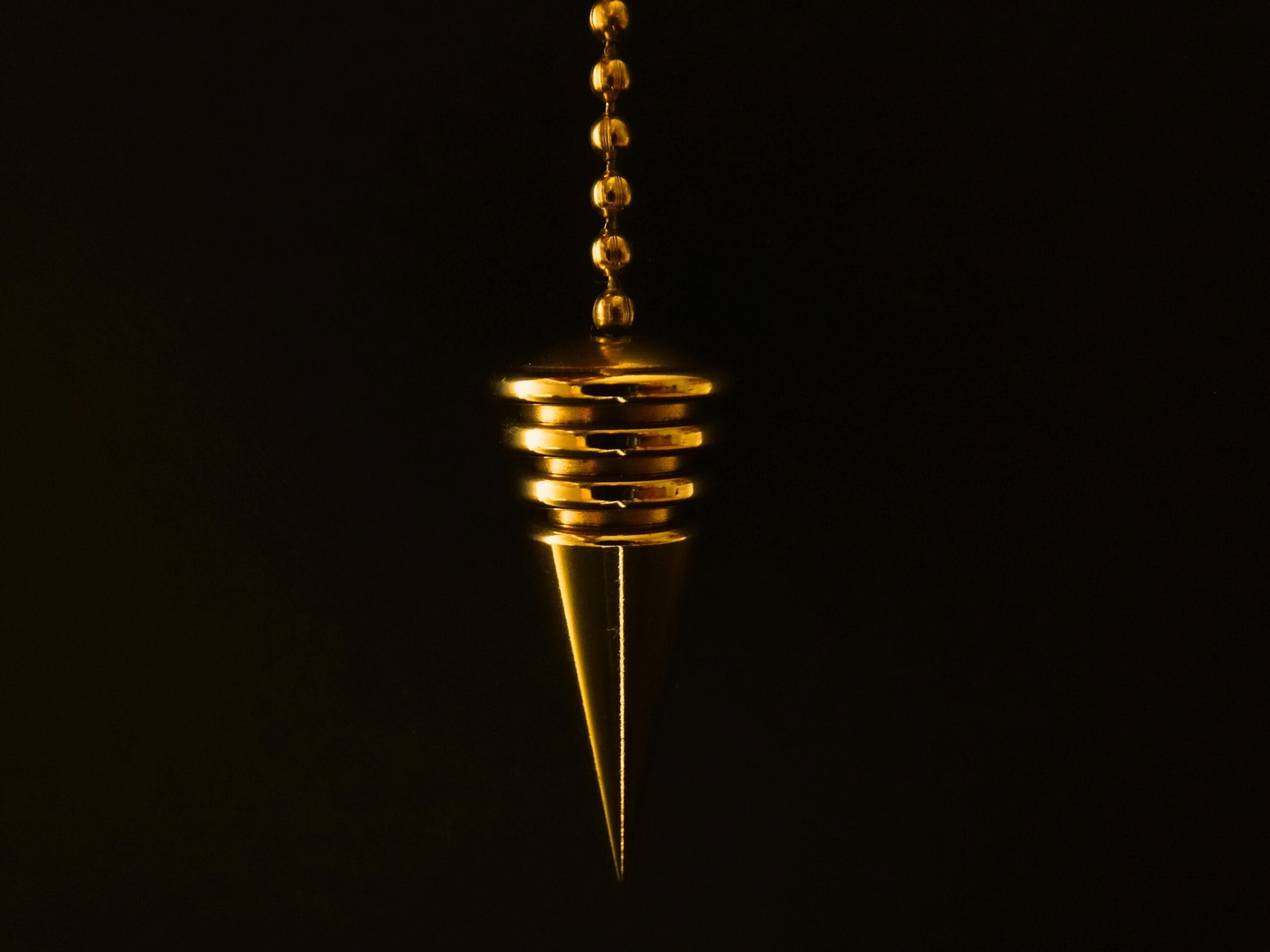 An elegant gold pendulum with chain on a mysterious black background.