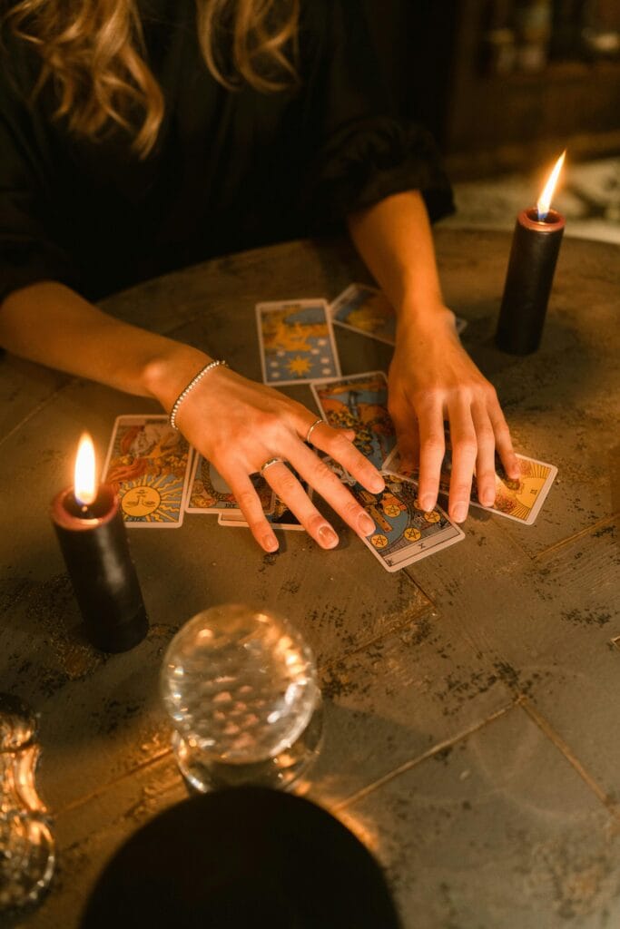 A woman engaging in a tarot card reading with candles and a crystal ball on a dimly lit table.